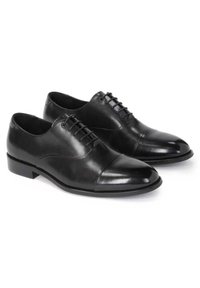 Paire de chaussures de ville Oxford en cuir noir poli avec laçage fermé et petit talon sur fond blanc.