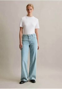 Biely rebrovaný top s krátkym rukávom skombinovaný so svetlomodrými širokými džínsami; hladké textúry, priliehavý top, vysoký pás a čierne topánky.