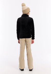 Zwarte fleecejas met een hoge kraag, gecombineerd met beige flared broeken. Een gebreide beige pet met een pompondetail maakt de outfit compleet.