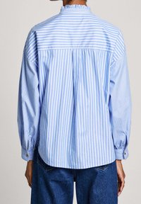 Light blue striped long-sleeve shirt with a high neck, gathered detail, and buttoned cuffs. Loose fit and soft fabric texture.