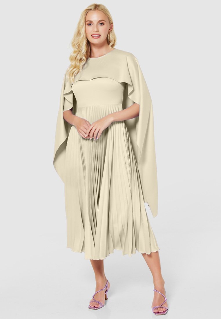 Plooi-midi jurk in lichtbeige met een ronde halslijn en gedrapeerde cape mouwen, gecombineerd met lavendelkleurige sandaaltjes met banden. Glad textuur.