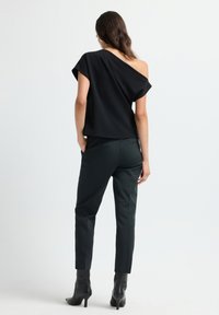 Top nero con spalle scoperte e vestibilità comoda, abbinato a pantaloni scuri su misura. Tessuto morbido e stivali aderenti alla caviglia completano il look.