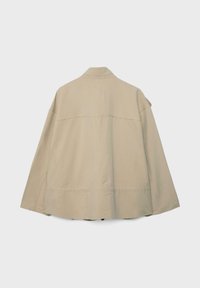 Veste beige à manches longues avec une coupe droite, couture de l'empiècement dos et détails de couture minimaux, vue de dos sur un fond uni.