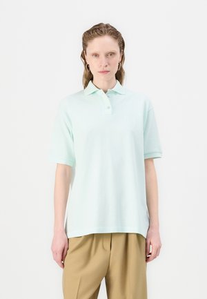 Tricou polo verde menta din bumbac, cu guler clasic, mâneci scurte și o croială lejeră, fără modele proeminente.