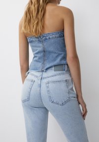 Top sin tirantes de mezclilla azul claro con cierre de cremallera en la espalda, combinado con jeans de tiro alto a juego en azul claro con bolsillos traseros.