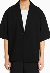 Mustakalla lyhythihainen takki, jossa on shaalikaulus, yksittäinen nappikiinnitys ja rento malli. Valmistettu sileästä, kevyestä kankaasta.
