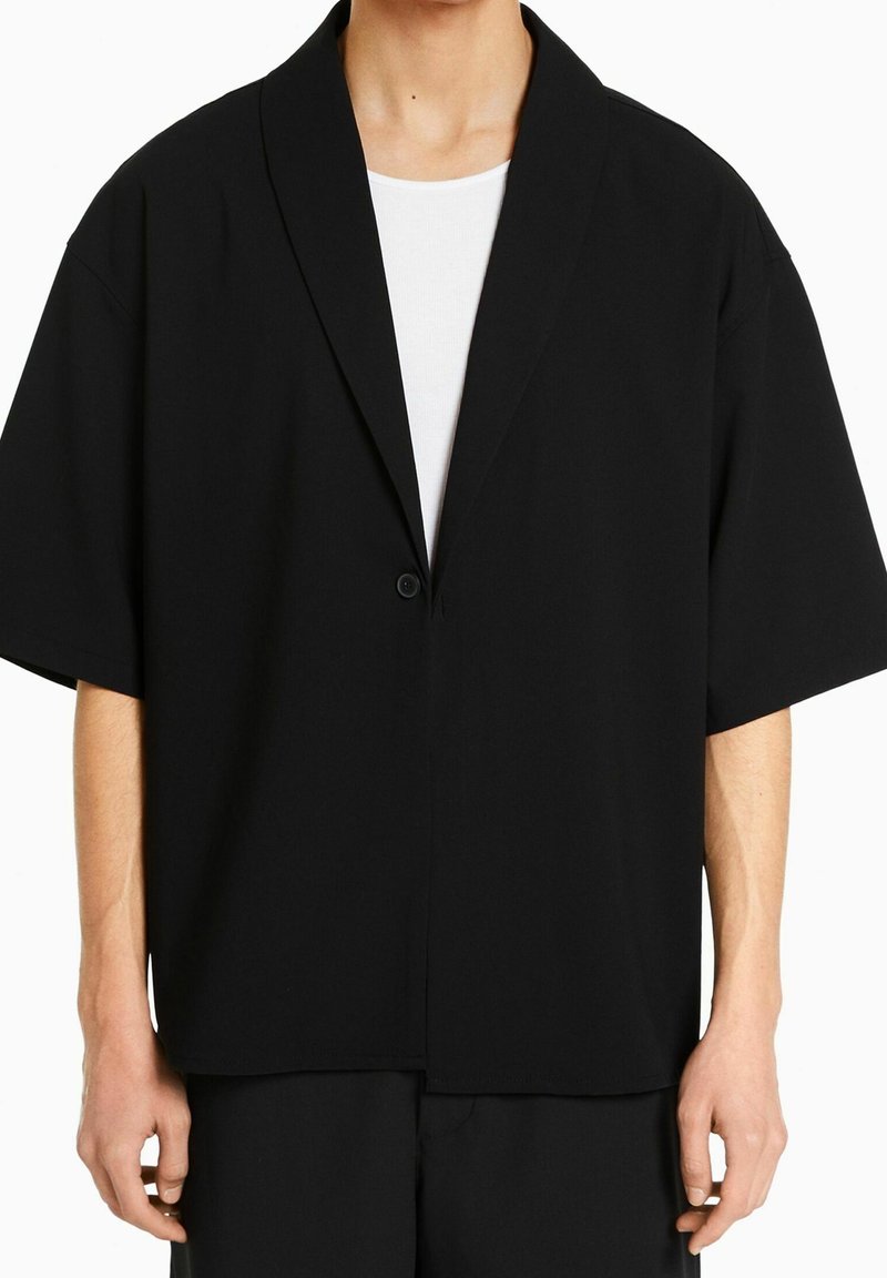 Mustakalla lyhythihainen takki, jossa on shaalikaulus, yksittäinen nappikiinnitys ja rento malli. Valmistettu sileästä, kevyestä kankaasta.