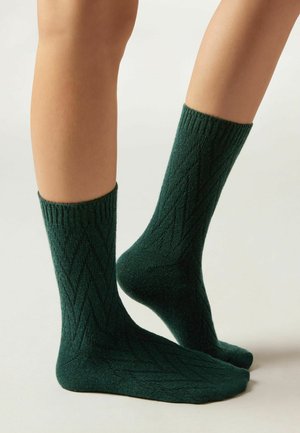 Mörkgröna ankelsockor med en texturerad diamantmönster, ribbad mudd och mjukt ullblandat material.