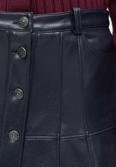 Tengerészkék bőrszoknya, testhezálló szabással, látható varrásokkal és négy gombos záródással. Különlegességei közé tartoznak az oldalzsebek és a derékpánt hurkok.