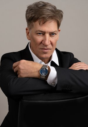 Montre en métal argenté avec un cadran bleu, un motif texturé et des accents argentés. Portée à un poignet vêtu d'un costume noir et d'une chemise blanche.