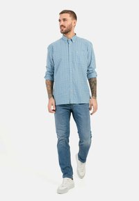 Blauw-wit geruit overhemd met lange mouwen opgerold, gecombineerd met lichtblauwe jeans en witte sneakers. Eenvoudige, casual outfit.