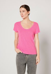 Camiseta rosa de manga corta con escote redondeado. Fabricada con un tejido ligero y texturizado. Combinada con jeans de talle alto grises.