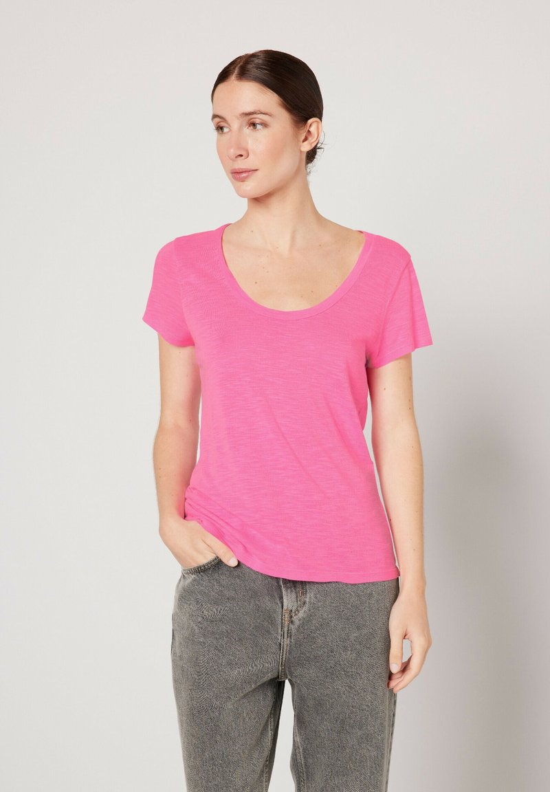 Camiseta rosa de manga corta con escote redondeado. Fabricada con un tejido ligero y texturizado. Combinada con jeans de talle alto grises.