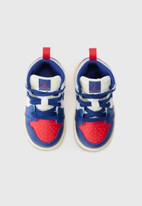 Zapatilla azul y roja con acentos perforados en rojo, puntera blanca, cordones negros y una lengüeta roja. Presenta un logo en la lengüeta.