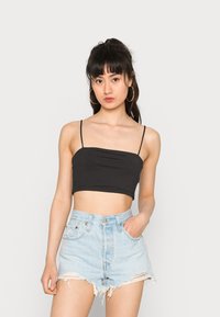 Top cropped preto com alças finas, combinado com calções de ganga claros de cintura alta com bordas desfiadas e um bolso frontal.