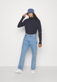 Maglione a collo alto navy, jeans a vita alta azzurri e cappello a secchiello blu. I jeans presentano una linea dritta e dettagli di cucitura discreti.