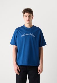Mėlynas medvilninis marškinėlis trumpomis rankovėmis, apvaliu kaklu, su baltai išsiuvinėtu užrašu "calvin klein" ant priekio. Dėvimi su tamsiomis kelnėmis.