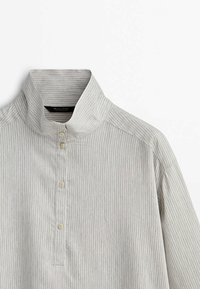 Chemise gris clair avec fines rayures verticales, col montant et quatre boutons blancs au centre devant.