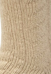 Kremowa, dziergana skarpetka o teksturowanym wzorze, z delikatnymi złotymi nitkami splecionymi w tkaninie jako ozdobny akcent.