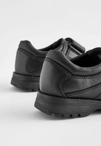Chaussures en cuir noir à profil bas et surface texturée. Présentent une couture renforcée et une semelle en caoutchouc avec un motif de traction.