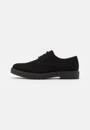 Chaussure en daim noir avec un bout arrondi, un design à lacets plats et une semelle extérieure texturée dotée de petites grips uniformes pour une traction optimale.