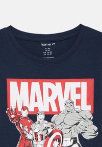 T-shirt de algodão azul-marinho com um grande logótipo "MARVEL" em vermelho e branco, apresentando personagens de desenhos animados como o Iron Man, o Capitão América e o Hulk.
