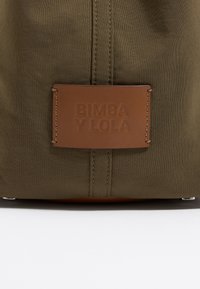 Olijfgroene stoffen tas met een bruine leren label, geperst met "BIMBA Y LOLA." Voorzien van stikdetails en metalen hardware accenten.