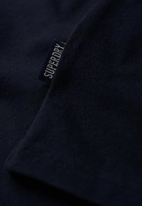 Mørk marineblå stof med et lille syet mærke, der viser "SUPERDRY" i hvide store bogstaver.
