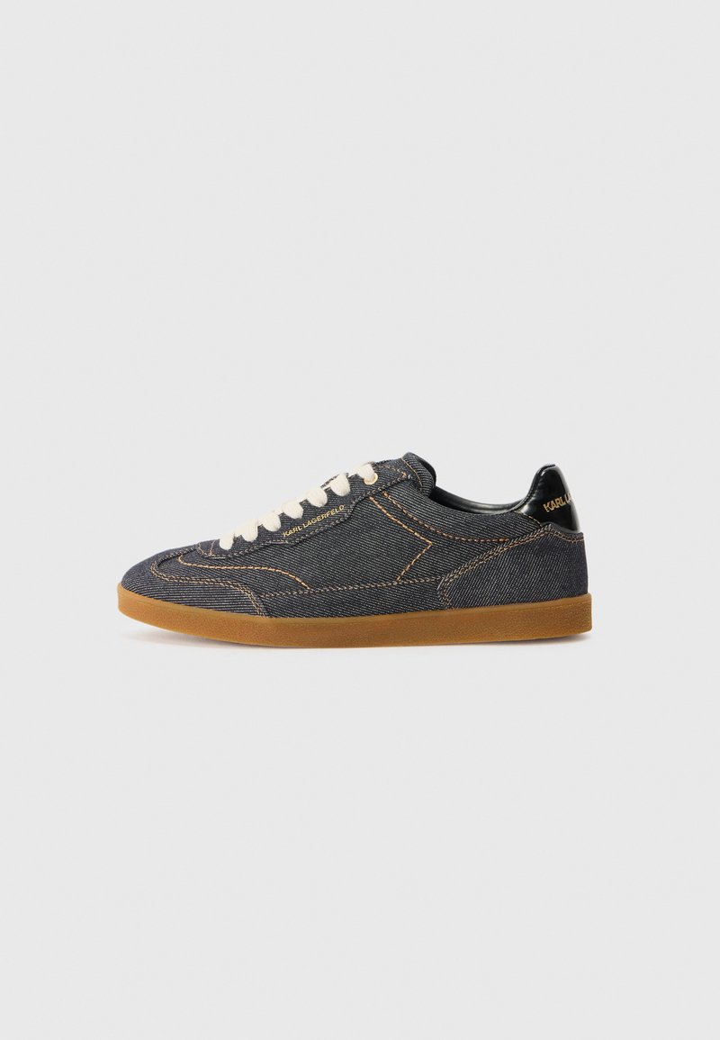 Sapatilhas de denim com um cabedal azul escuro, costuras laranja em contraste e uma sola de borracha crepe. Apresentam atacadores brancos e um detalhe em preto no calcanhar.