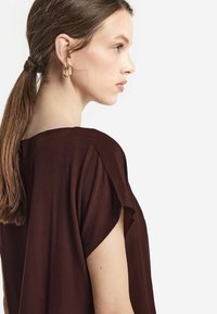 Brun kortärmad topp med lös passform, med rundad halsringning och mjuk, slät textur. Guldörhängen i form av hoops som utmärkande detaljer.