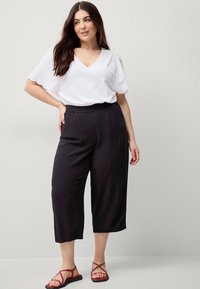 Blusa bianca in cotone con scollo a V e maniche ricamate a scallop, abbinata a pantaloni cropped neri plissettati e sandali rossi con cinturini.