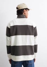 Csíkos pulóver fehér és sötétzöld árnyalatokban, magas gallérral és bordás mandzsettákkal. Puha pamut anyag, laza fazonnal.