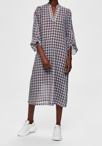 Ruudullinen mekko sinisessä ja ruskeassa, valmistettu läpikuultavasta kankaasta. Ominaisuuksiin kuuluu V-pääntie ja kolme neljäsosaa hihat, yhdistetty valkoisiin tennareihin.