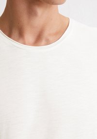 Weißes T-Shirt mit Rundhalsausschnitt aus einem weichen, gerippten Material, gefertigt aus leichtem Stoff mit einer subtilen Textur.
