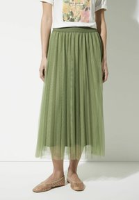 Green tulle maxi skirt with layered pleats; elastic waistband. Worn with nude ballet flats featuring silver studs.
