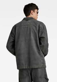 Siva denim jakna z ohlapnim krojem, ki ima razpeta ovratnika, dolge rokave in vidne šive. Brez sprednjega zapiranja, enostaven dizajn.