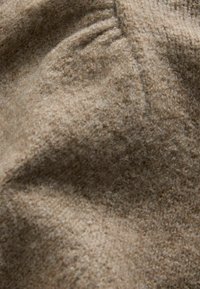 Miękka, brązowa, teksturowana tkanina wełniana z widocznymi włóknami i szczegółowym, misternym splotem, widziana z bliska.