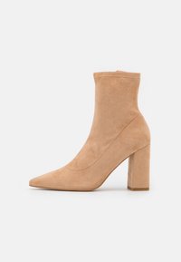 Stivale alla caviglia in suede beige con punta affusolata, tacco alto a blocco e design senza cuciture. Texture liscia con dettagli di cucitura minimi.