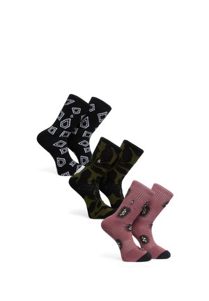 Trois paires de chaussettes hautes à motifs : une noire avec des formes géométriques blanches, une camouflage verte et noire, et une rose poudré avec des motifs noirs et jaunes.