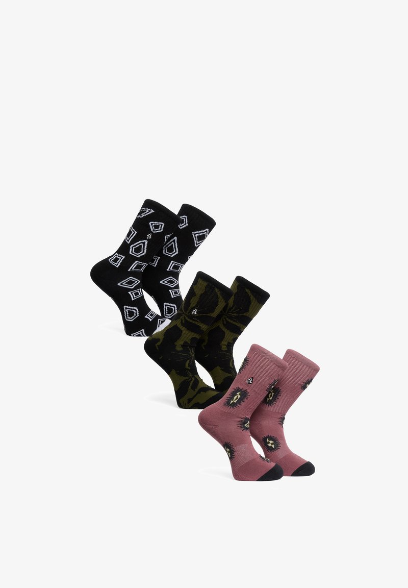Trois paires de chaussettes hautes à motifs : une noire avec des formes géométriques blanches, une camouflage verte et noire, et une rose poudré avec des motifs noirs et jaunes.