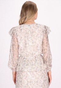Bloemmotief jurk van lichte, doorzichtige stof met franje mouwen en een elastische taille. Zachte kleuren in perzik, crème en subtiele groentinten.