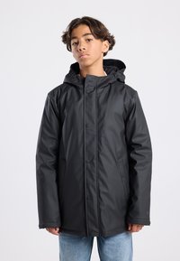Black waterproof jacket with a hood, featuring snap closures, side pockets, and a smooth, shiny texture. Worn over blue jeans.