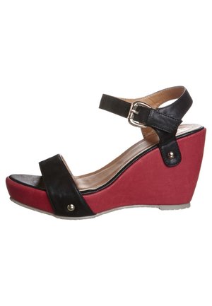 Czarno-czerwony sandał na koturnie z paskiem na kostkę, charakteryzujący się teksturowaną czarną skórzaną cholewką, czerwoną platformą oraz metalowymi akcentami z boku.