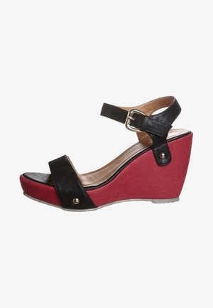 Sandalía tipo cuña negra y roja con tiras en el tobillo, que presenta una parte superior de cuero negro texturizado, plataforma roja y acentos metálicos en el lateral.