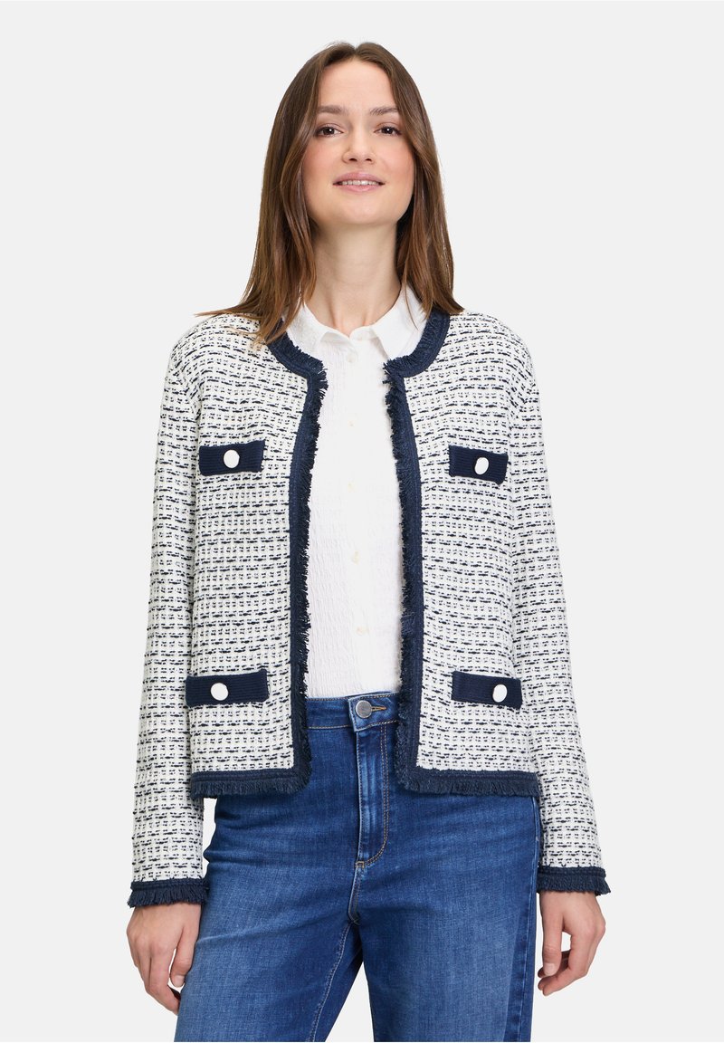 Weißer und marinefarbener Tweed-Blazer mit fransigen Kanten, runden, marinefarbenen Knöpfen und aufgesetzten Taschen. Über einem weißen Hemd getragen, mit blauem Jeans.