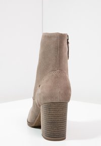Botín de ante en beige claro con un tacón de madera texturizada. Cuenta con una cremallera lateral y un detalle de costura sutil.