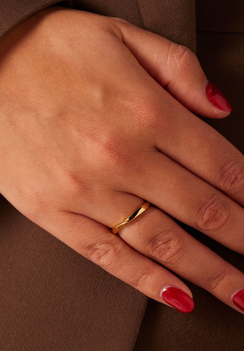 Gouden ring met een gepolijste afwerking, met een gladde band en subtiel geometrisch ontwerp, gedragen aan een hand met rode nagellak.