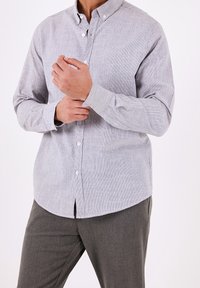 Ljusgrå knäppt skjorta med ett fint strukturerat mönster, lång ärm och krage, kombinerad med mörkgrå byxor.