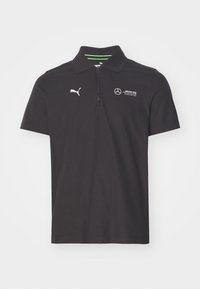 Polo noir avec un col zippé, présentant des logos blancs : Puma sur la poitrine gauche et Mercedes sur la droite. Détails verts à l'intérieur du col.
