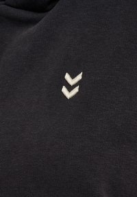 Twee witte geborduurde chevrons op zwarte stof, gecentreerd en verticaal gepositioneerd.